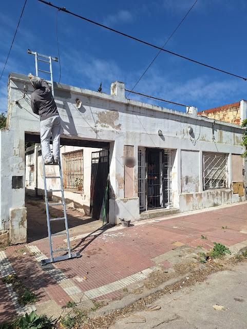 Frente de una vivienda con la pintura deteriorada y un técnico sobre una escalera comenzando el trabajo