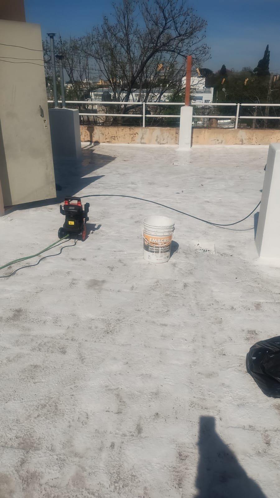 Techo plano durante un trabajo de impermeabilización, con una hidrolavadora y un balde de impermeabilizante